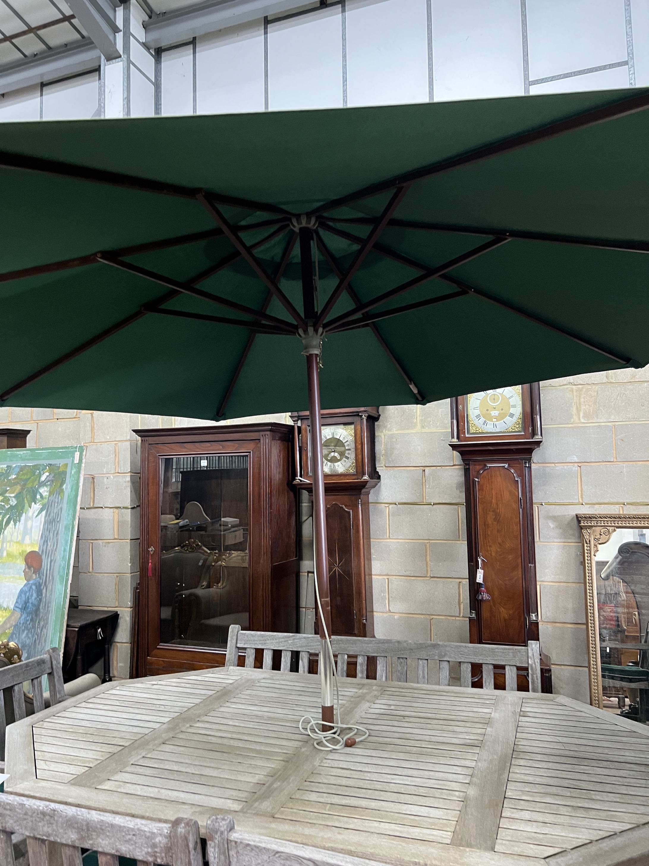 An Alexandra Rose weathered teak octagonal garden table, length 210cm, width 122cm, height 74cm, a bench, four elbow chairs with seat pads, and a green canvas parasol with cast metal base